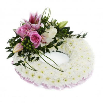 Pink Wreath Based with Spray - A traditional wreath of massed white Chrysanthemums with a corsage of flowers in Pink blooms. Edges with ribbon. 

Please note images are examples only, flowers used may vary due to seasonal availability.

This item requires 3 days notice to order.