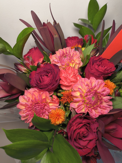 Scarlet Daydream - A bold and beautiful bouquet bursting with rich scarlet roses, vibrant pink and orange blooms, and striking seasonal foliage. Scarlet Daydream combines deep romantic tones with pla